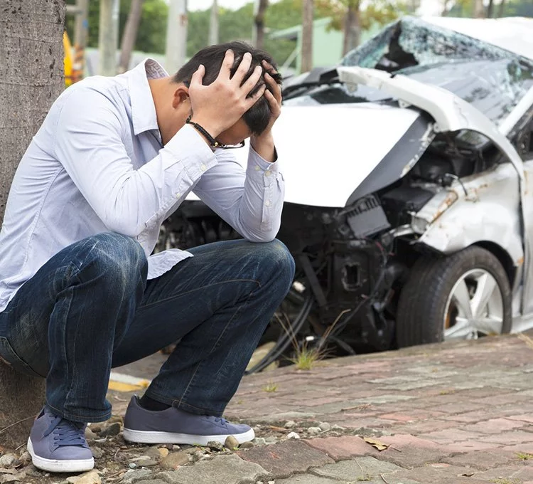 Immediately after a car crash, a man with confusion is sitting in the pathway with hands-on his heads